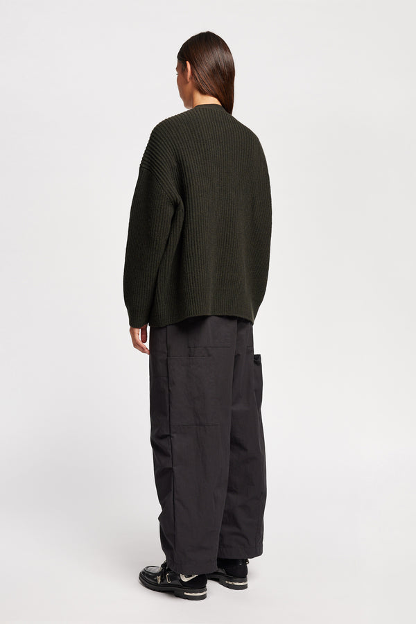 Back angle view of model wearing oversized ribbed wool cardigan with button closure in darkest green
