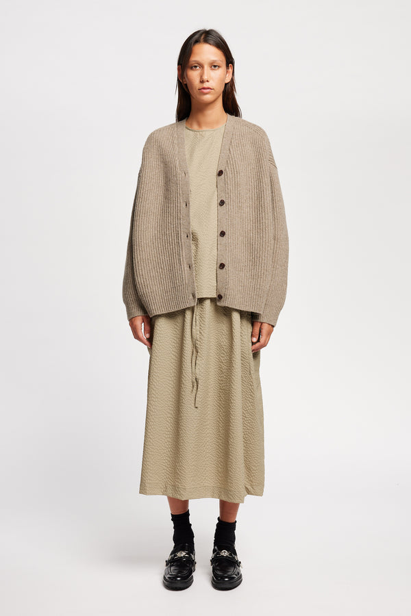 Front view of model wearing oversized ribbed wool cardigan with button closure in light taupe
