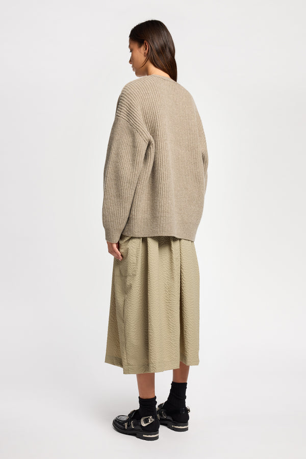 Back angle view of model wearing oversized ribbed wool cardigan with button closure in light taupe