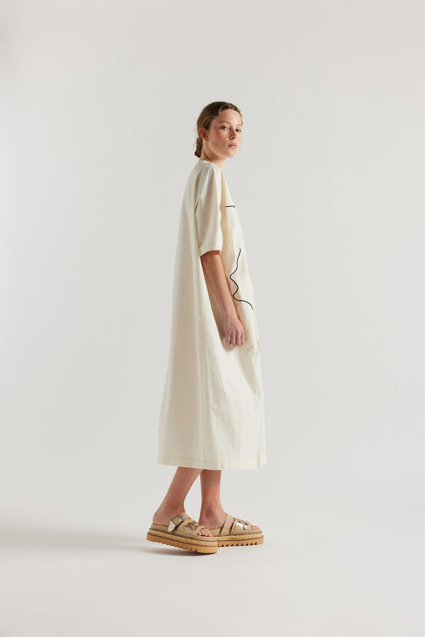 side view of female model in the ecru Pensive Dress with black embroidered motifs and round neckline