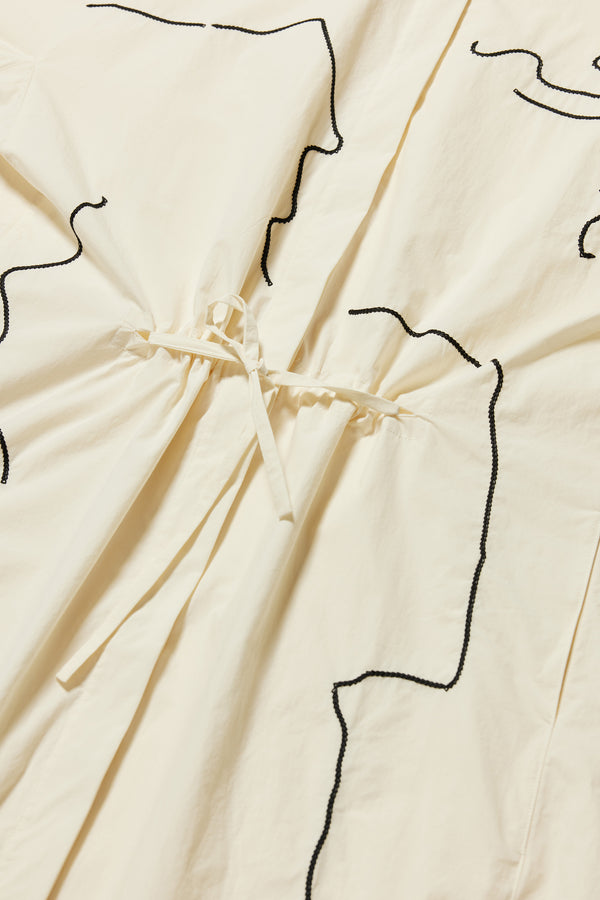 details shot of the ecru Pensive Dress with black embroidered motifs and highlighting the encased self tie waist 