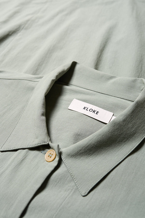 Close up details of the Plein Long Sleeve Shirt in Olive Green. An oversized panel shirt with a cocoon back, front tuck, and pleated dropped sleeves, can be styled as a lightweight jacket.