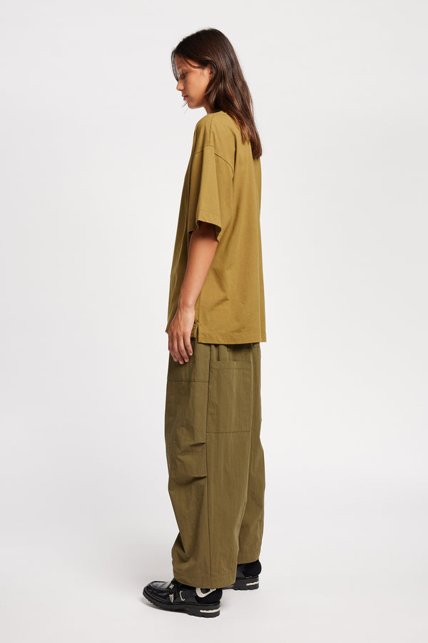 Back of Model wearing the Premise Cargo in Kelp Green, a relaxed-fit pant with adjustable waistband, clean front pleats, and straight-leg silhouette.