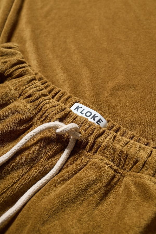 Detail view of the purple Oeko-Tex certified coffee brown cotton terry  + encased elastic waistband and adjustable cord tie on slouchy track pants.