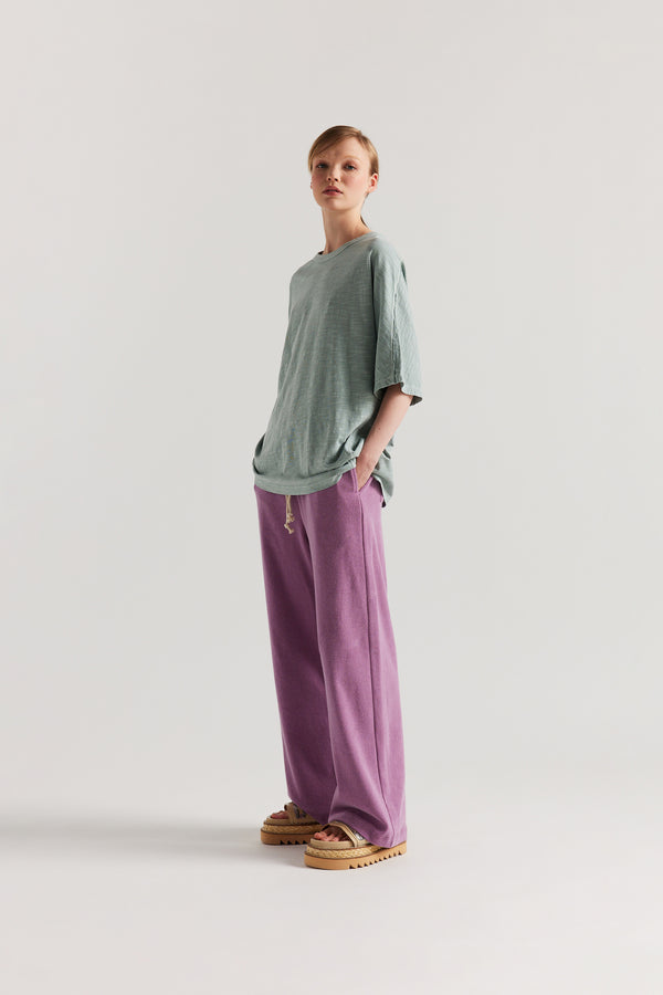 Front view of slouchy track pants in purple cotton terry with straight-leg fit and cord-tie waistband.