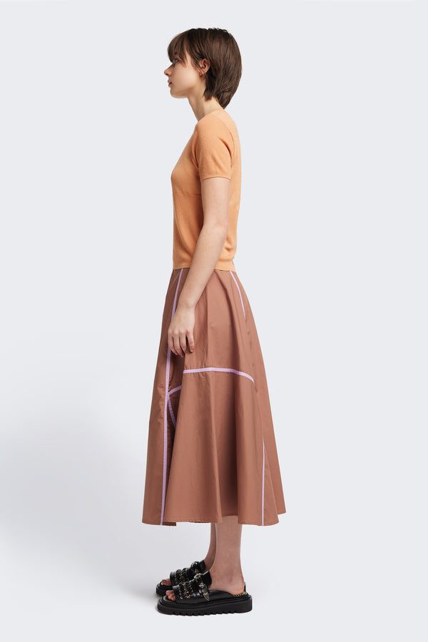 side of the brown/lilac Regarder Bound Skirt in a lightweight cotton fabric, featuring a fuller silhouette with contrast bound seam details, midi length, and a back invisible zip closure.