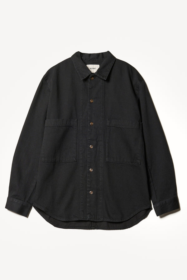 Flat front shot of the Region oversized denim shirt in Black, featuring utility chest pockets