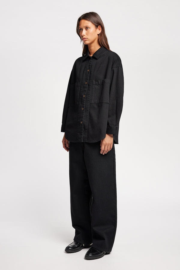 Front angle view of model wearing the Region oversized denim shirt in Black, featuring utility chest pockets.