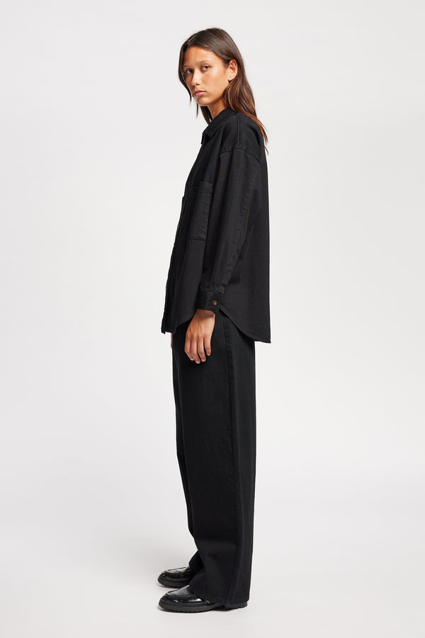 Side view of model wearing the Region oversized denim shirt in Black, featuring utility chest pockets.