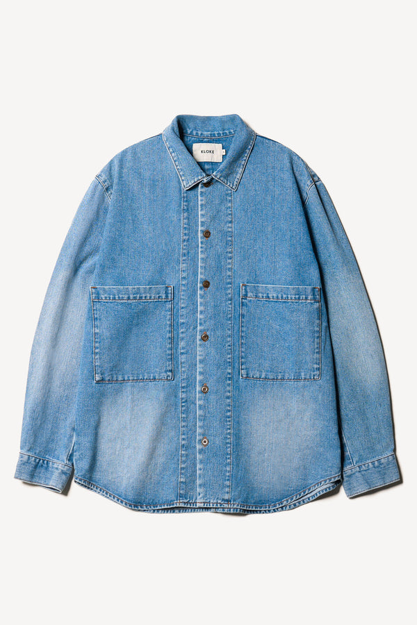 Flat Front view of the Region oversized denim shirt in mid-blue, featuring utility chest pockets.