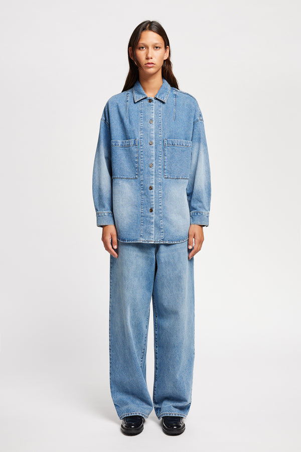Front view of model wearing the Region oversized denim shirt in mid-blue, featuring utility chest pockets.