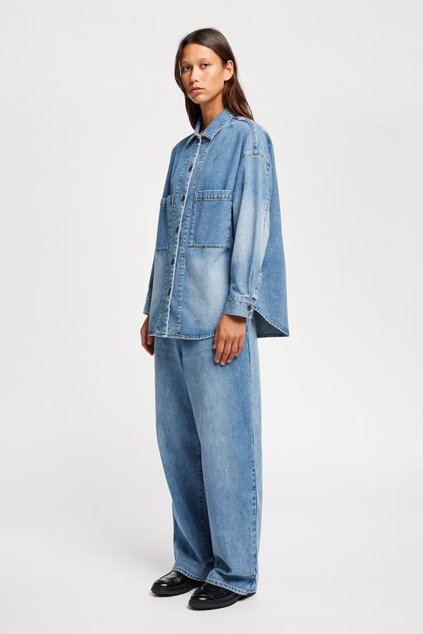 Front angle view of model wearing the Region oversized denim shirt in mid-blue, featuring utility chest pockets.