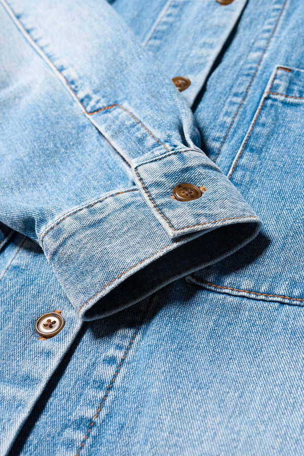 Close up detail cuff and button shot of the Region oversized denim shirt in mid-blue, featuring utility chest pockets.