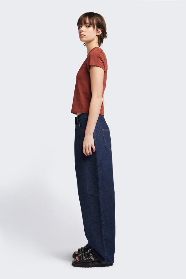 Side view of the model in The Reset Jean Indigo is a relaxed baggy jean featuring two darts at the centre front waistline and darts across the knee.  