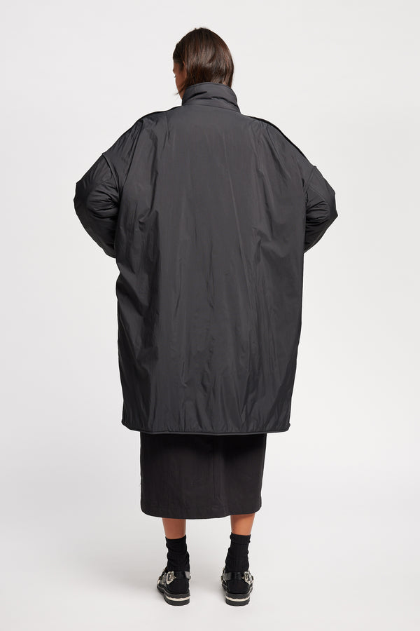 Back view on model of the oversized Restore Coat in Black, showcasing  relaxed silhouette and clean lines