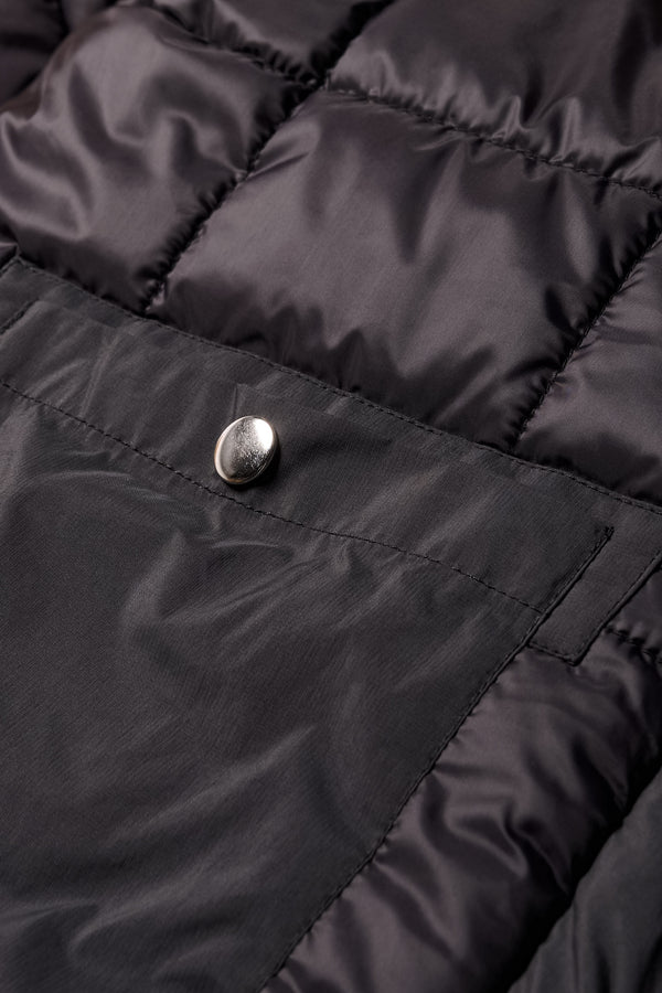 Close-up of zip stud button closure on inside pocket and quilted texture on the Restore Coat in black