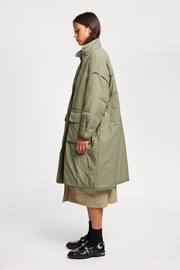Side view on model of the oversized Restore Coat in Dusty Olive Green, showcasing  relaxed silhouette and clean lines