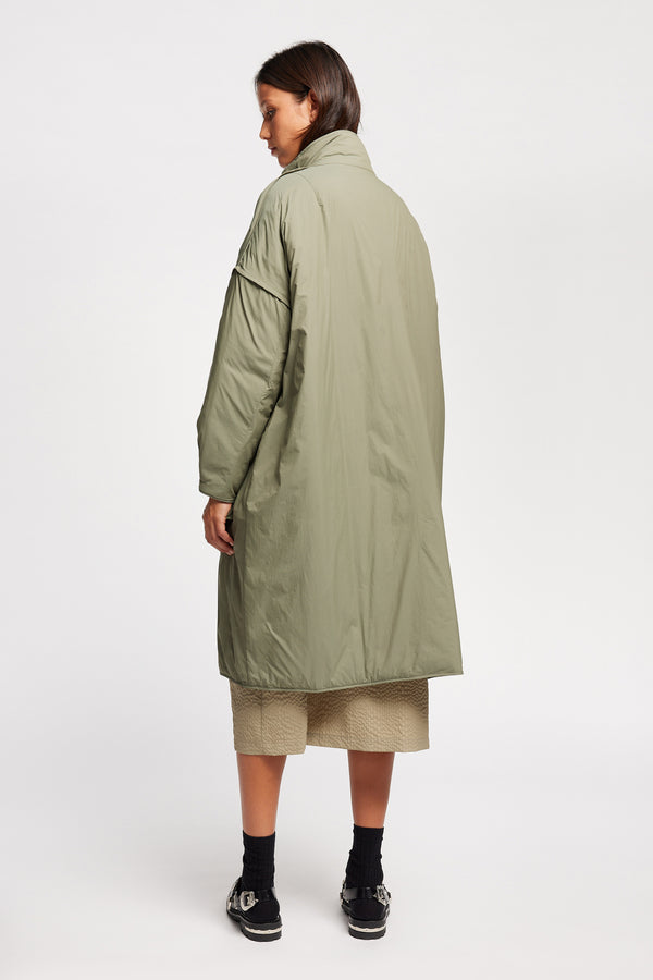 Back view on model of the oversized Restore Coat in Dusty Olive Green, showcasing  relaxed silhouette and clean lines