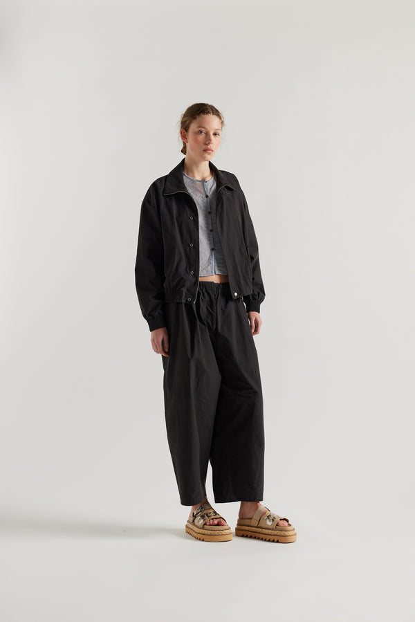 Front view of model in the black slate Reverie Jacket showing two-way zip closure and topstitched welt pockets.