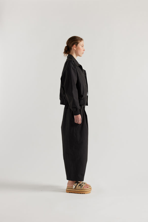 Side view of model in the black slate Reverie Jacket showing two-way zip closure and topstitched welt pockets.
