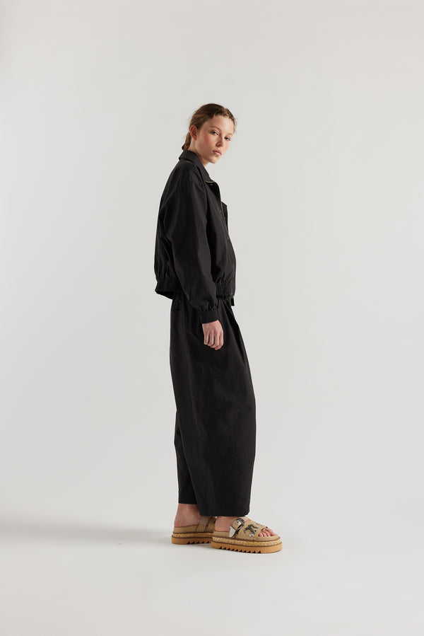 Side view of model in the black slate Reverie Jacket showing two-way zip closure and topstitched welt pockets.