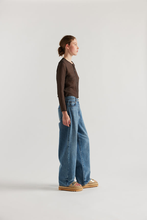 Side View of model in the Rising LS Shirt in Brown. A slim-fitting long sleeve shirt with rounded self-bind collar and straight hem.