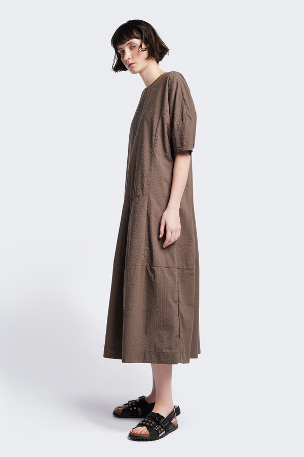 Side of the Scoria Dress in brown, a long-panelled cotton seersucker dress with voluminous sleeves, structured panel details, and a fuller skirt, perfect for an effortless summer look. Available in 5 sizes. 