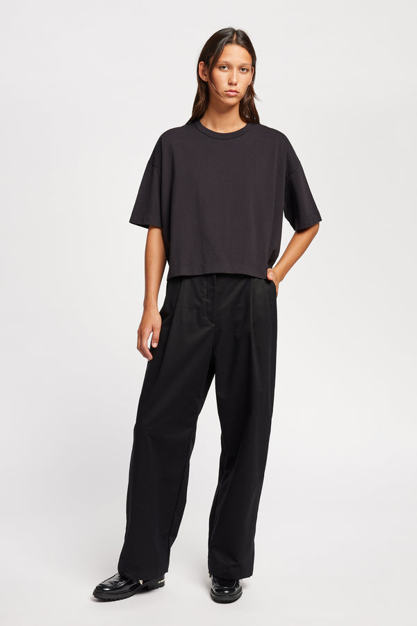 Front of Model wearing Seleno pants in black with a relaxed, tapered leg and pleat detailing, styled with Obelisk Tee in Black.