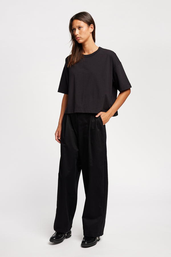 Front of Model wearing Seleno pants in black with a relaxed, tapered leg and pleat detailing, styled with Obelisk Tee in Black.