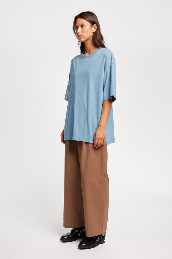 Front of Model wearing Seleno pants in clay brown with a relaxed, tapered leg and pleat detailing, styled with Monolith Tee in Blue.