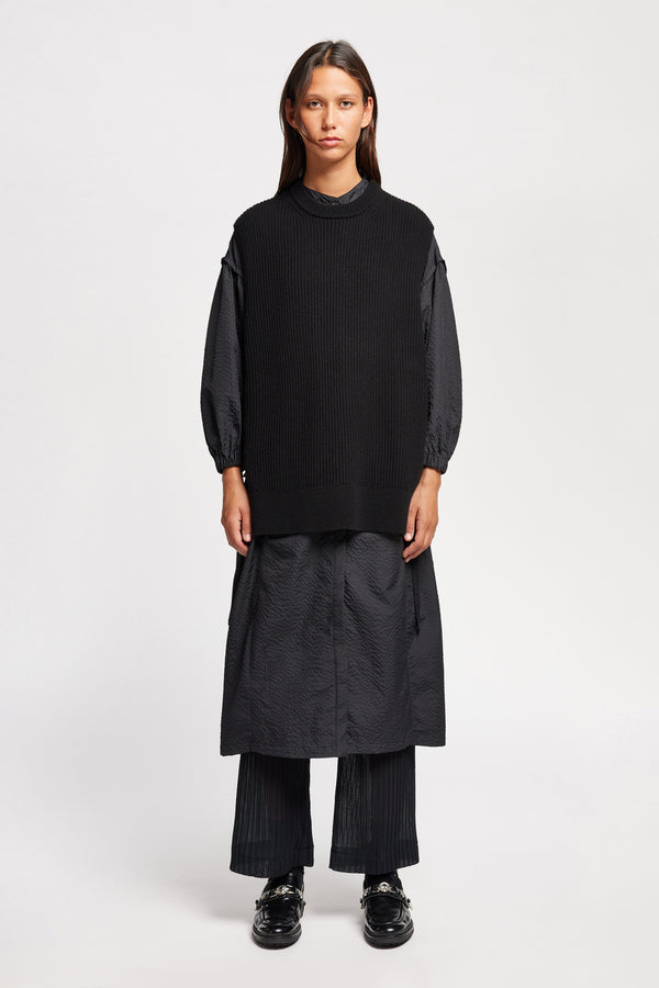 Front view of model wearing the black sleeveless ribbed knit vest with side ties in merino and cotton blend