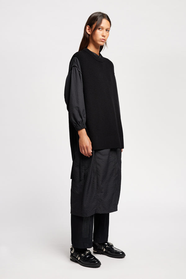 Front angle view of model wearing the black sleeveless ribbed knit vest with side ties in merino and cotton blend