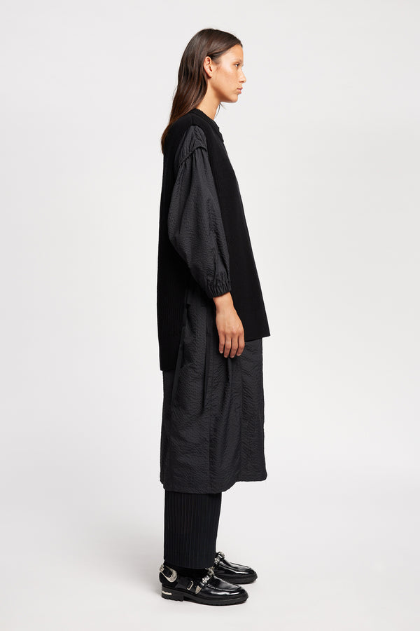 Side view of model wearing the black sleeveless ribbed knit vest with side ties in merino and cotton blend