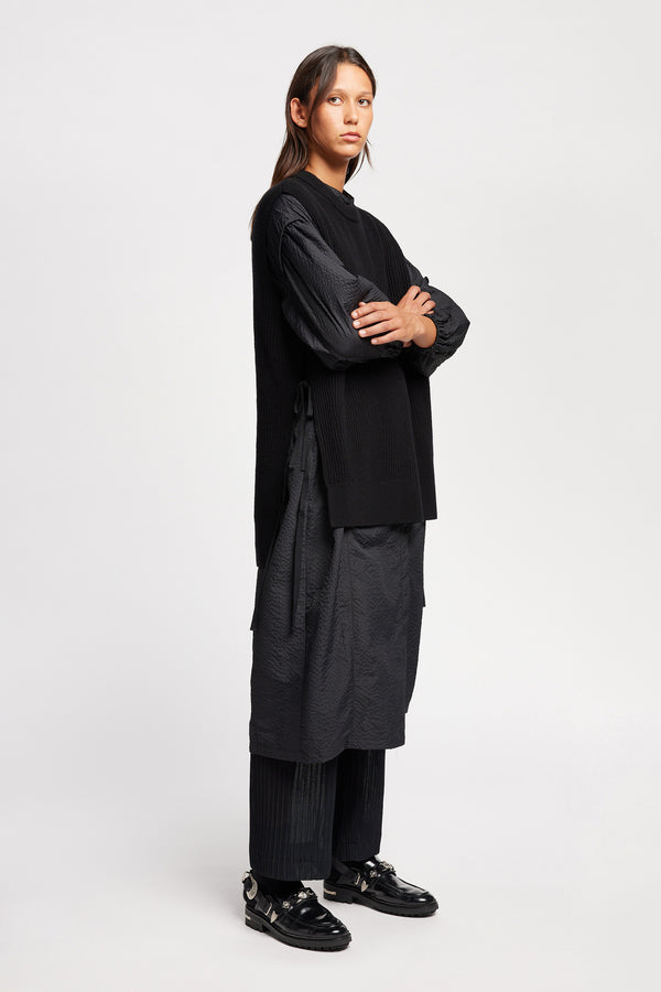 Front angle view of model wearing the black sleeveless ribbed knit vest with side ties in merino and cotton blend