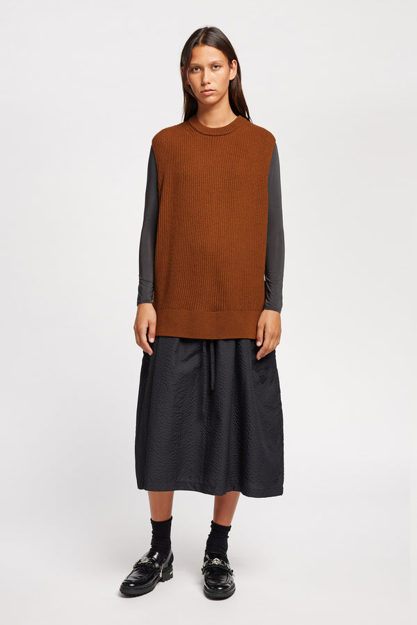 Front view of model wearing toffee brown sleeveless ribbed knit vest with side ties in merino and cotton blend