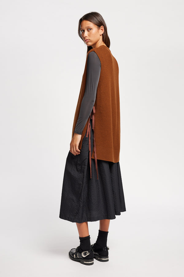 Back angle view of model wearing toffee brown sleeveless ribbed knit vest with side ties in merino and cotton blend