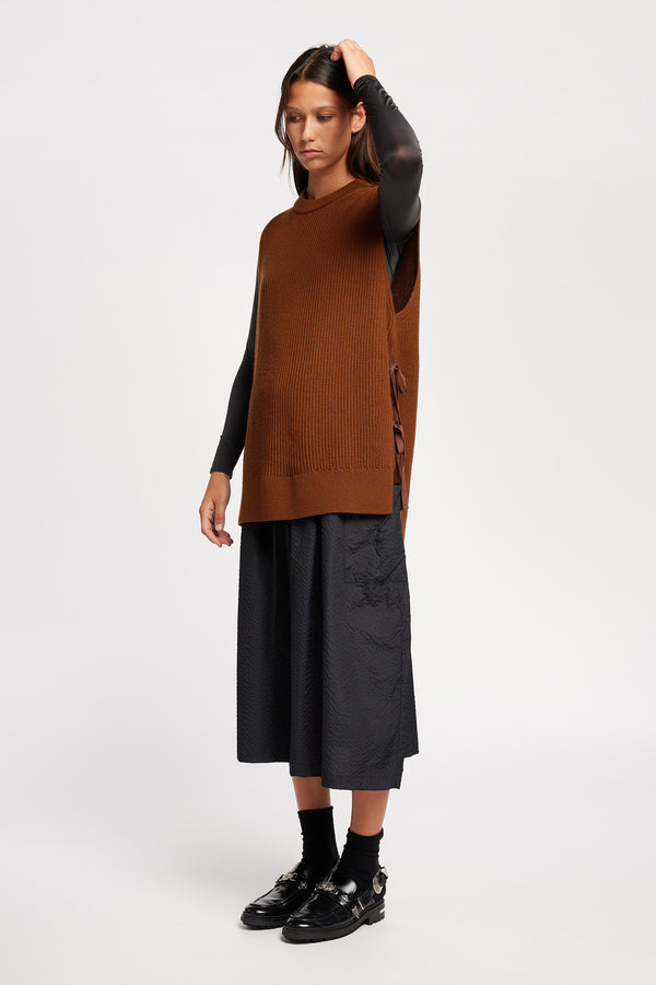 Front angle view of model wearing toffee brown sleeveless ribbed knit vest with side ties in merino and cotton blend
