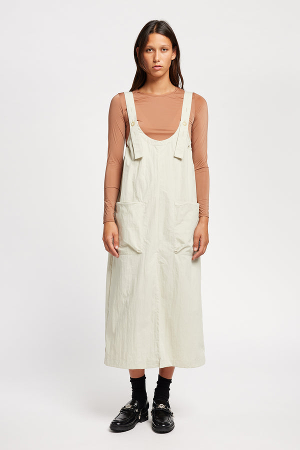 Font of the model wearing the Shoreline full-length pinafore dress in bone white with deep round neckline and front patch pockets, a relaxed-fit silhouette. 