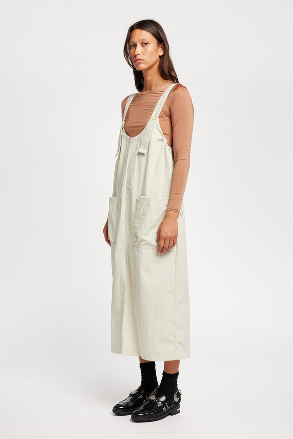 Font of the model wearing the Shoreline full-length pinafore dress in bone white with deep round neckline and front patch pockets, a relaxed-fit silhouette. 