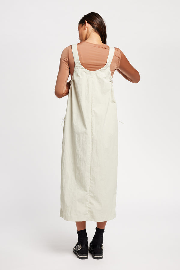 Back of the model wearing the Shoreline full-length pinafore dress in bone white with deep round neckline and front patch pockets, a relaxed-fit silhouette. 