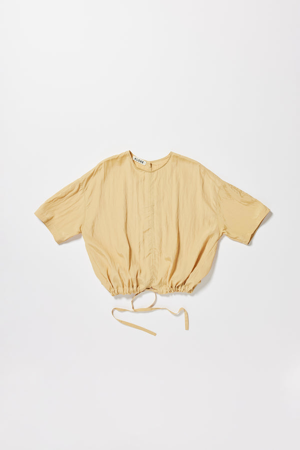 Flat front of the sand beige Stillness Top with round neckline and centre front seam detail. Showing cinched at hem with the self tie. 