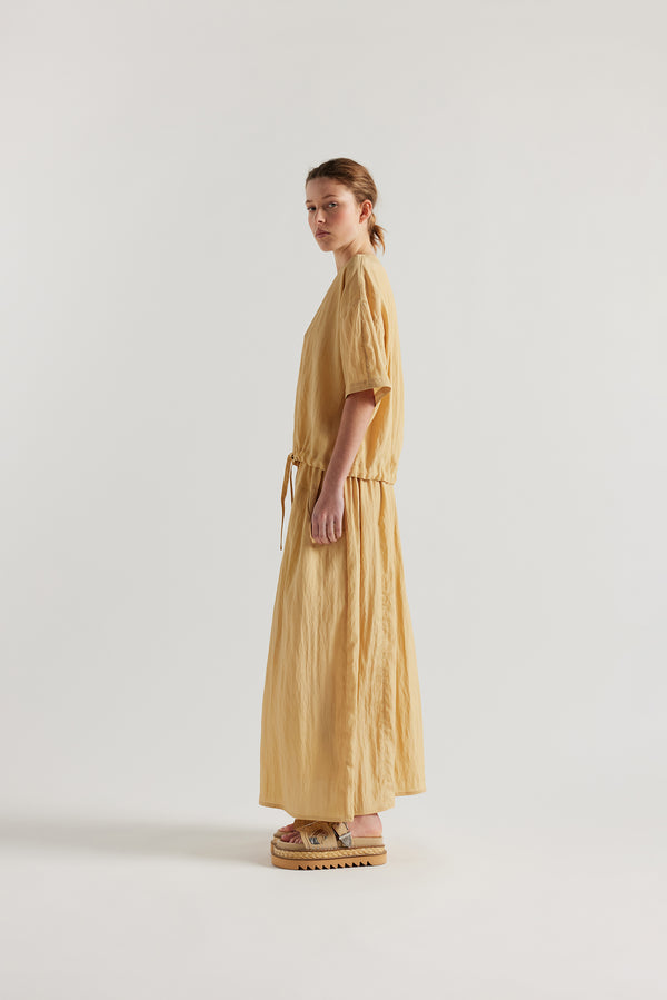 Side of model in the sand beige Stillness Top with round neckline and centre front seam detail.