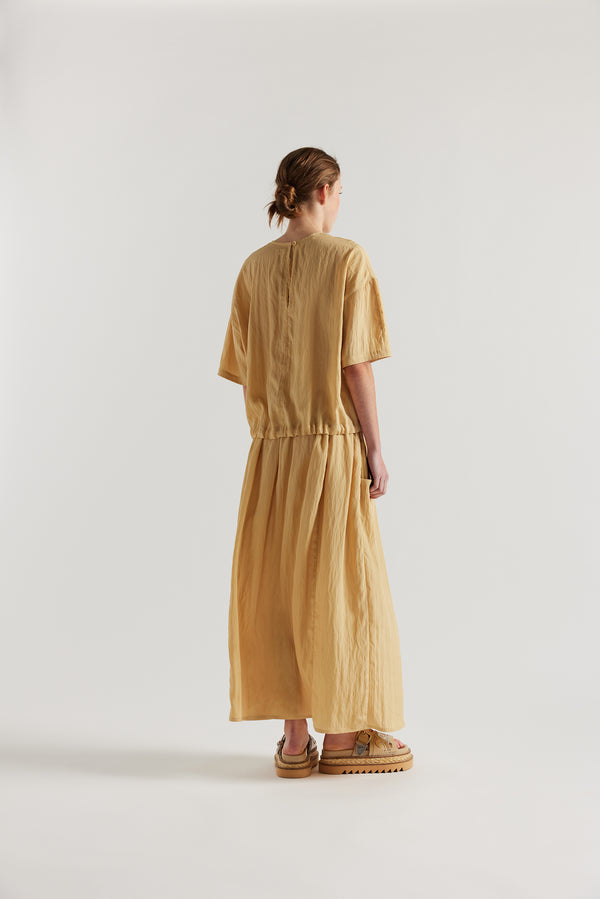 back of model in the sand beige Stillness Top with round neckline and centre front seam detail.