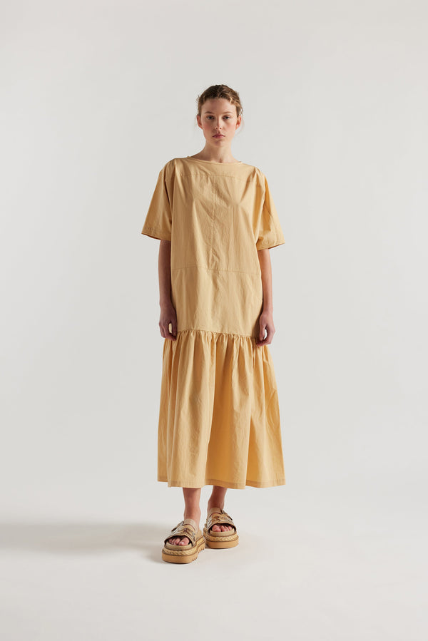 Front view of model wearing the Surrender Dress in sand showing panelled detailing, dropped waist, and gathered skirt. 