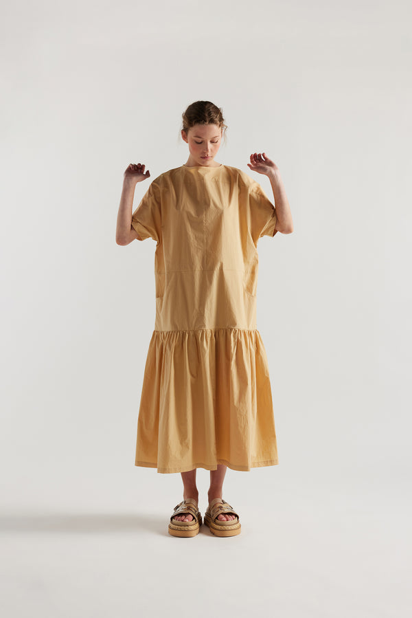 front view of model wearing the Surrender Dress in sand showing panelled detailing, dropped waist, and gathered skirt. 