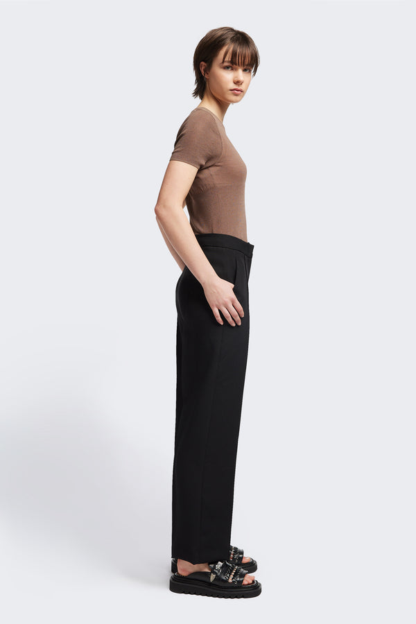 Side view of the Tranquillity Pant in black, a slim-fit stovepipe-style tailored pant with pin tuck detailing.
