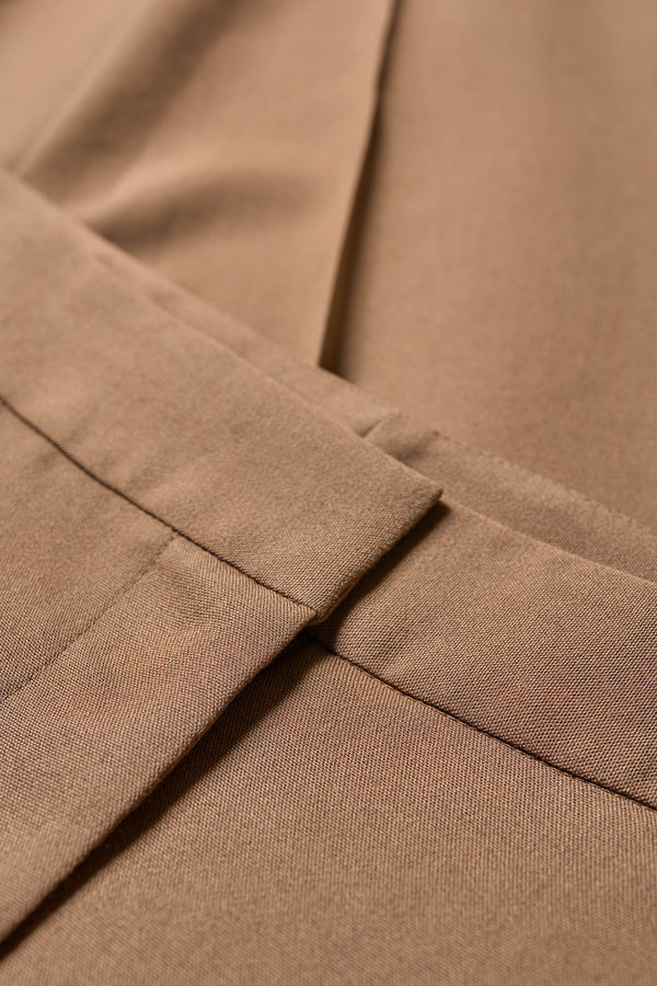 close up detail shot of the Tranquillity Pant in brown, a slim-fit stovepipe-style tailored pant with pin tuck detailing.