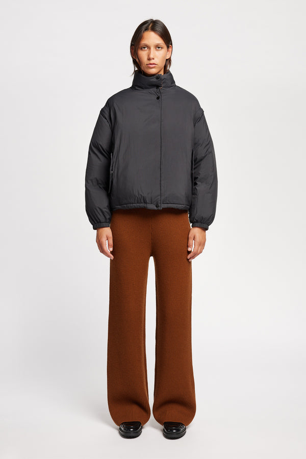 Front of Model wearing the Transform Puffa Jacket in black with sleeves attached, zipped up, showcasing cropped length and high collar