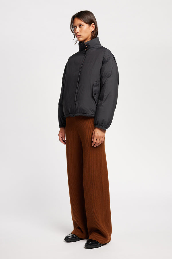 Model wearing the Transform Puffa Jacket in black with sleeves attached, zipped up, showcasing cropped length and high collar