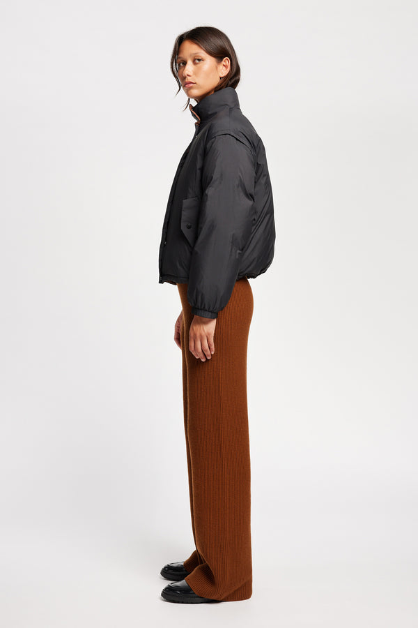 Side view of Model wearing the Transform Puffa Jacket in black with sleeves attached, zipped up, showcasing cropped length and high collar